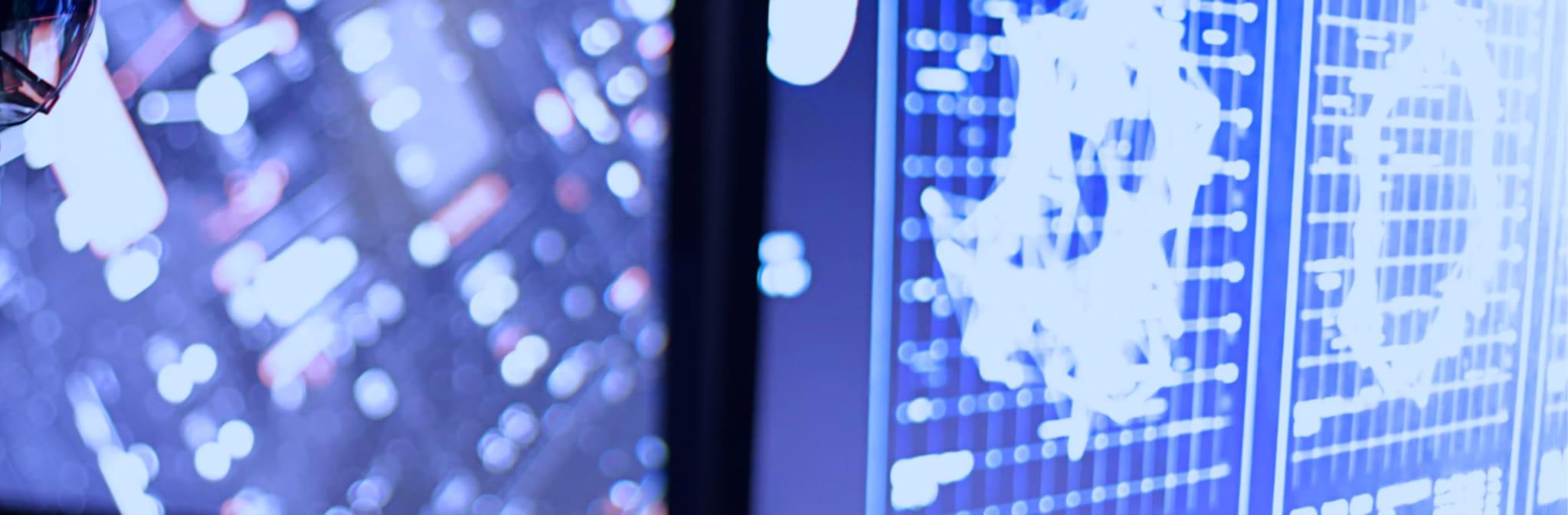 Blurred blue circuit lights beside monitors showing data grids